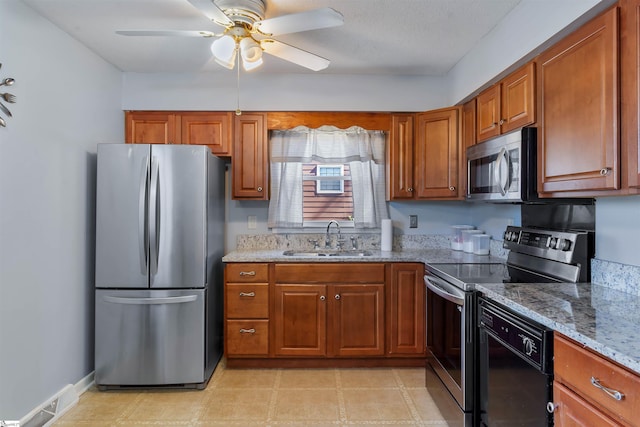 kitchen featuring light stone countertops, brown cabinetry, stainless steel appliances, and a sink