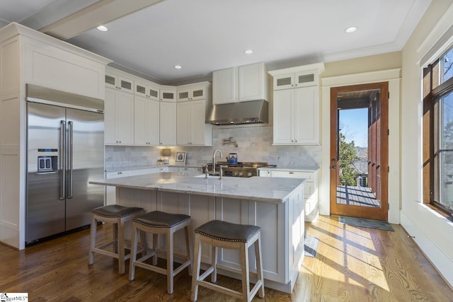 kitchen with under cabinet range hood, backsplash, wood finished floors, and built in fridge