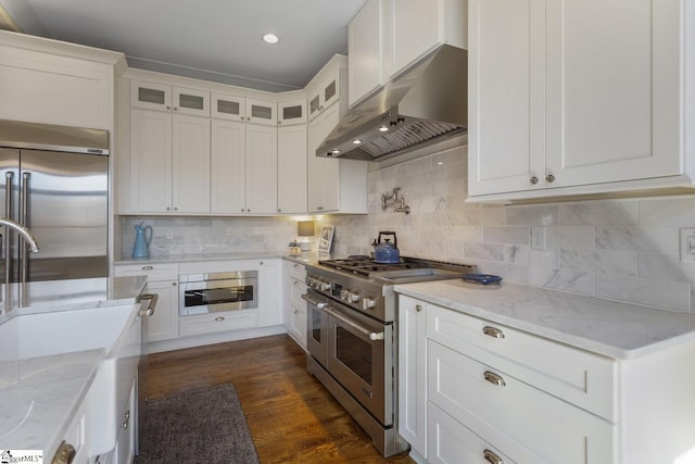 kitchen featuring high end appliances, tasteful backsplash, dark wood-type flooring, glass insert cabinets, and under cabinet range hood