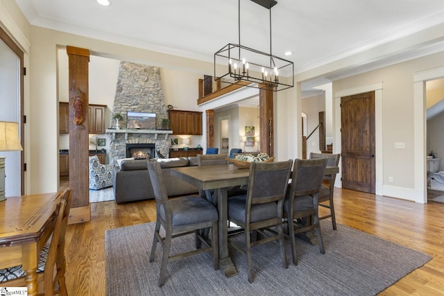 dining room featuring light wood finished floors, ornamental molding, and a stone fireplace