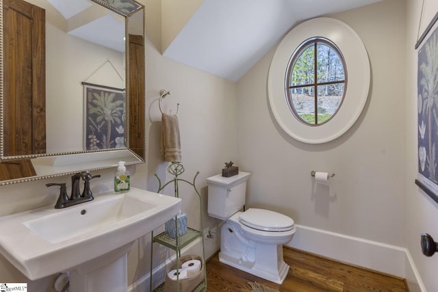 half bathroom featuring lofted ceiling, toilet, a sink, wood finished floors, and baseboards