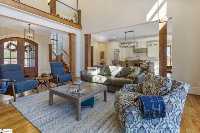 living room with light wood-style flooring, a notable chandelier, stairs, ornamental molding, and french doors