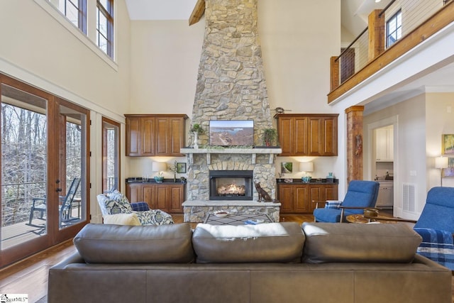 living room featuring a stone fireplace, wood finished floors, visible vents, baseboards, and french doors