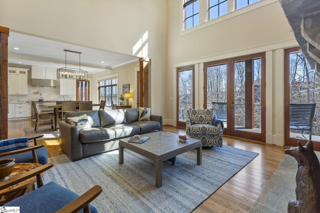 living room with plenty of natural light, light wood-style flooring, crown molding, and french doors