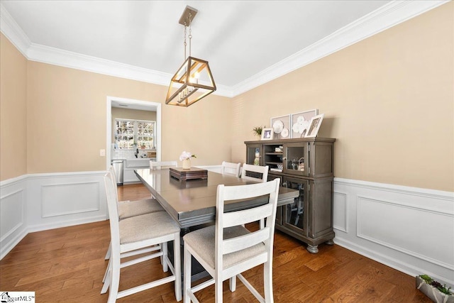 dining area with an inviting chandelier, ornamental molding, wood finished floors, and wainscoting