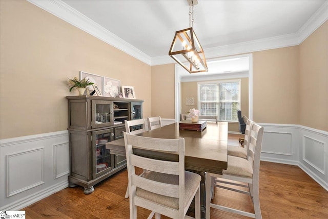 dining space with crown molding, wood finished floors, and wainscoting