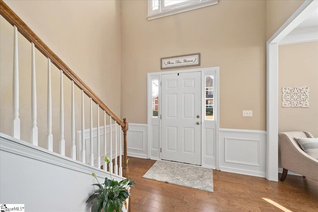 foyer entrance featuring hardwood / wood-style flooring, a decorative wall, a wainscoted wall, a towering ceiling, and stairway