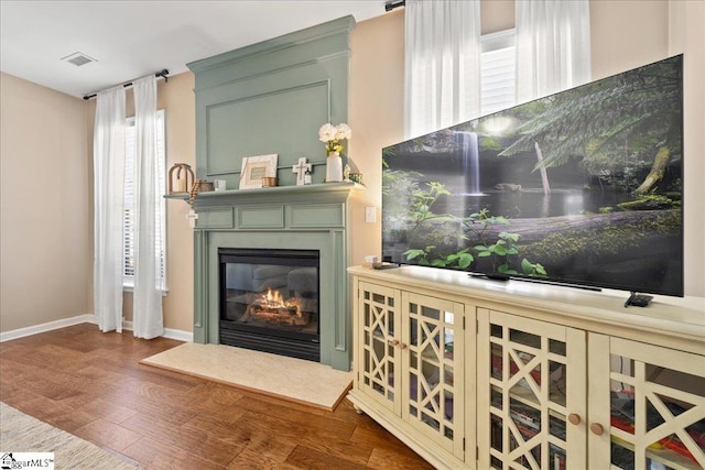 interior space featuring a large fireplace, visible vents, baseboards, and wood finished floors