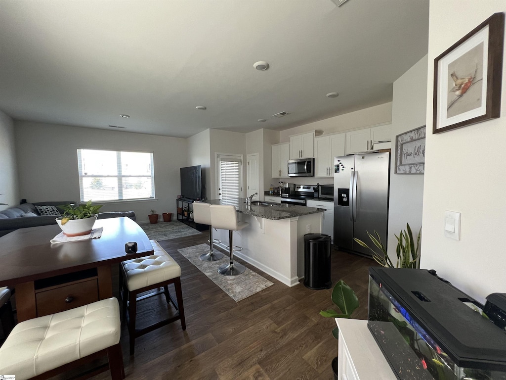 kitchen featuring appliances with stainless steel finishes, dark wood-type flooring, open floor plan, white cabinets, and a sink