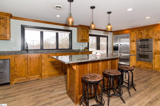 kitchen with visible vents, appliances with stainless steel finishes, brown cabinetry, a kitchen island, and a sink