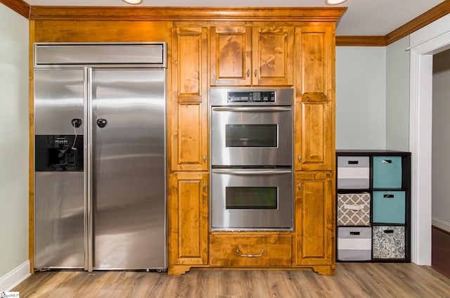 kitchen with brown cabinets, crown molding, stainless steel appliances, wood finished floors, and baseboards