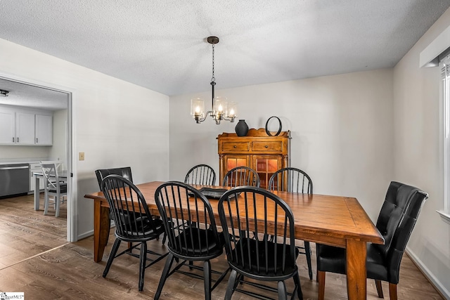 dining area featuring a textured ceiling, dark wood-style flooring, baseboards, and a notable chandelier