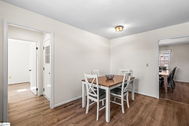 dining space with a textured ceiling, baseboards, and wood finished floors