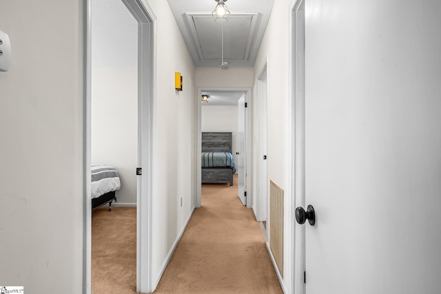 corridor featuring light carpet, attic access, and baseboards