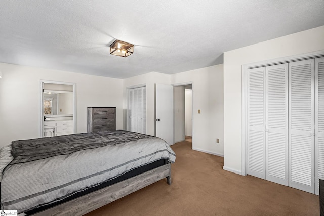 carpeted bedroom featuring multiple closets, baseboards, a textured ceiling, and ensuite bath