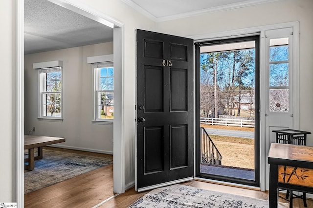 foyer entrance featuring crown molding, a textured ceiling, baseboards, and wood finished floors