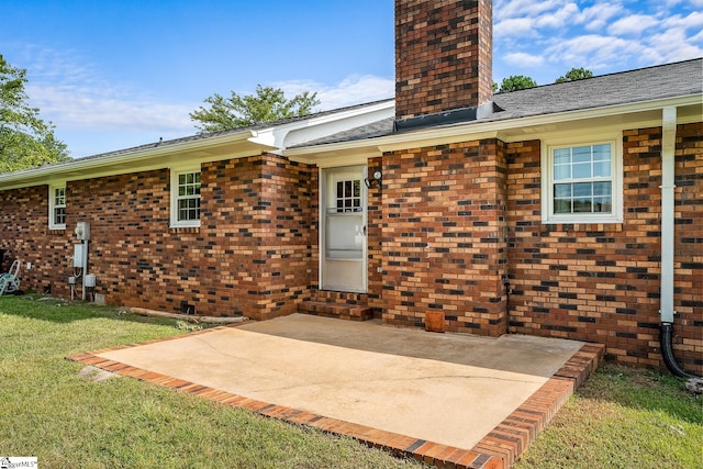 rear view of property with brick siding, a chimney, a lawn, and a patio