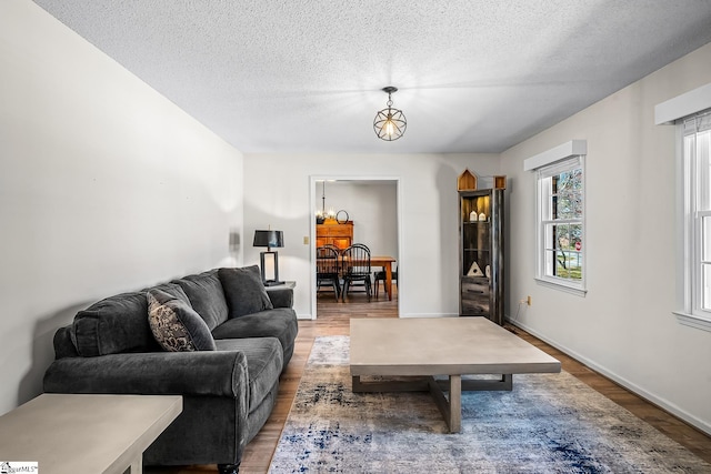 living room with a notable chandelier, a textured ceiling, baseboards, and wood finished floors