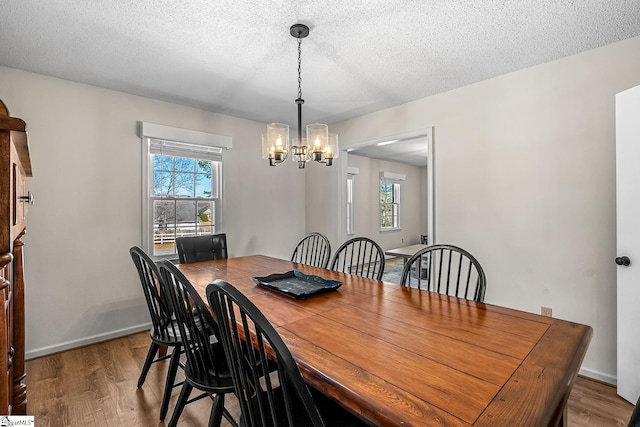 dining space featuring a chandelier, a textured ceiling, baseboards, and wood finished floors