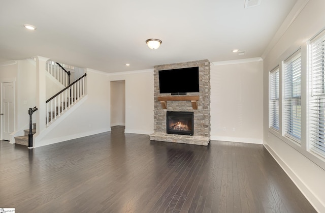 unfurnished living room with dark wood-style flooring, ornamental molding, a stone fireplace, baseboards, and stairs