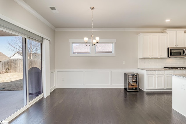 unfurnished dining area featuring wine cooler, a notable chandelier, a wainscoted wall, dark wood-style floors, and crown molding