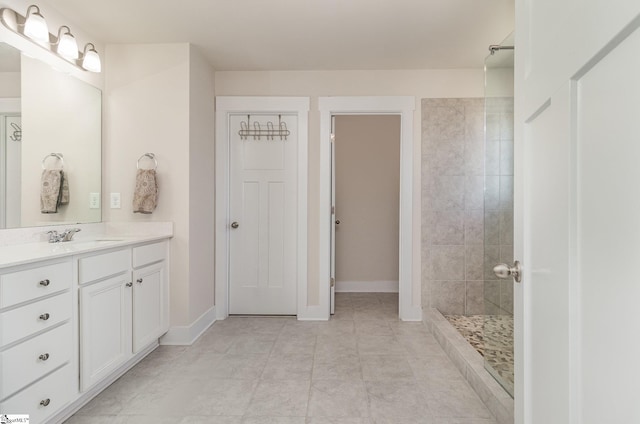 bathroom featuring a tile shower, vanity, and baseboards