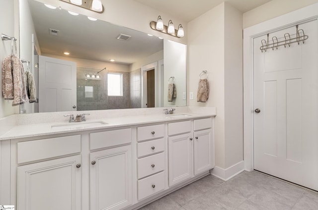 full bath with tiled shower, a sink, and visible vents