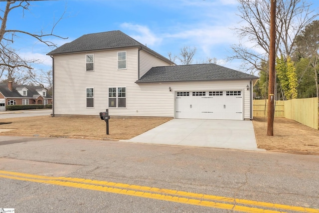 traditional home with a garage, concrete driveway, roof with shingles, and fence