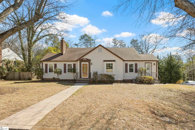 ranch-style home featuring a front lawn, a chimney, a shingled roof, and fence