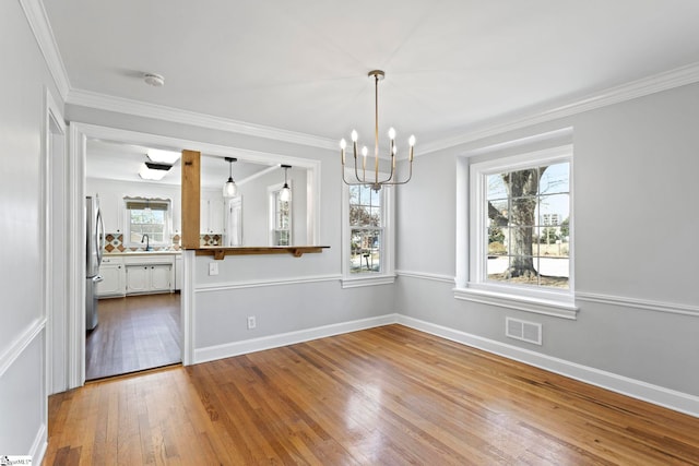 unfurnished dining area featuring baseboards, visible vents, hardwood / wood-style floors, crown molding, and a notable chandelier