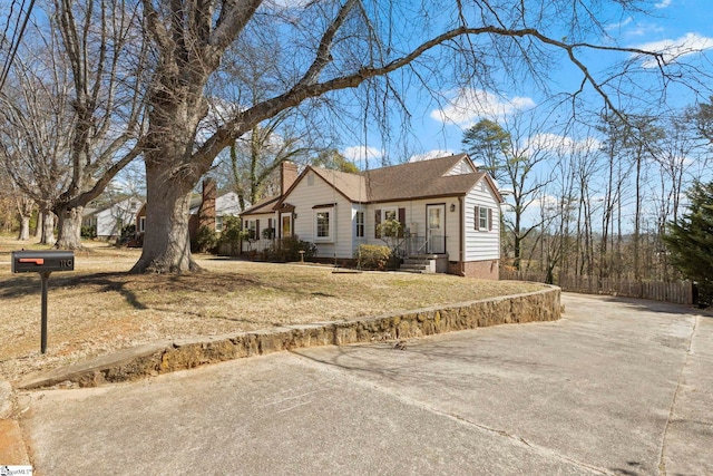 view of front of home with concrete driveway, a chimney, a front yard, and fence