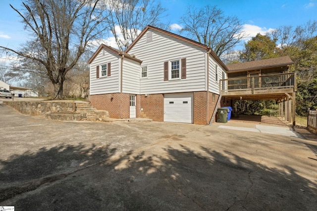 view of side of home featuring brick siding, concrete driveway, an attached garage, a deck, and stairs