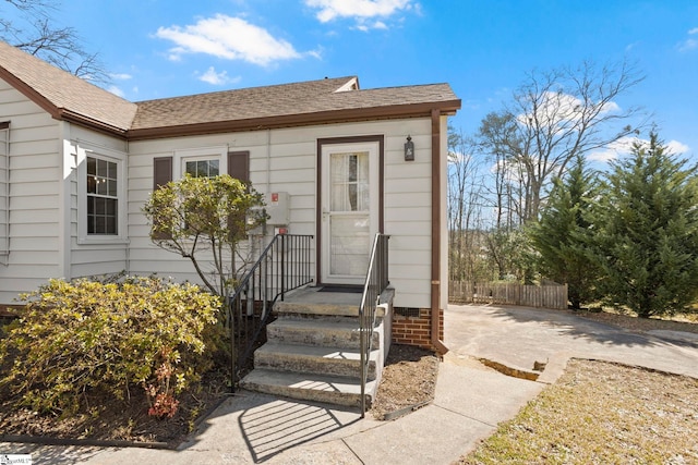 entrance to property featuring roof with shingles and fence