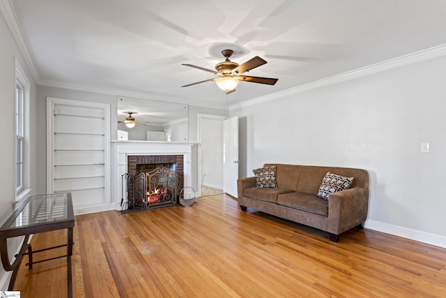 living room with baseboards, built in features, light wood-style floors, a brick fireplace, and crown molding