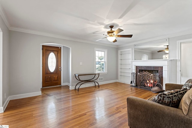 living room with arched walkways, crown molding, a fireplace, wood finished floors, and baseboards