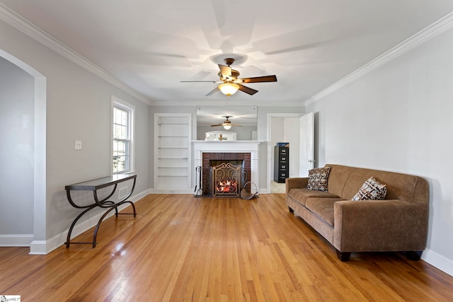 living area with light wood-type flooring, a brick fireplace, baseboards, and crown molding