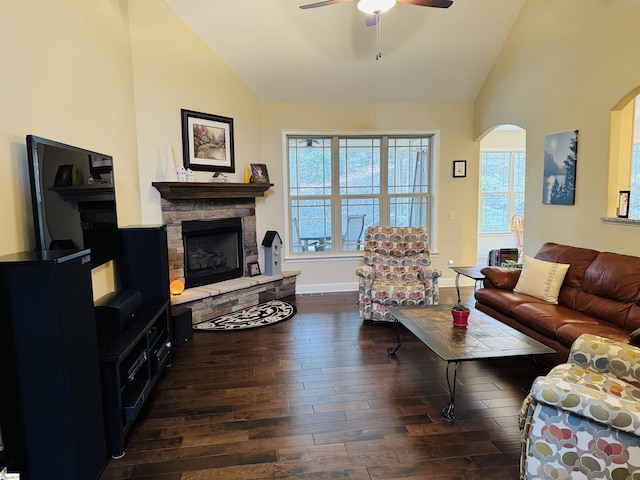 living room featuring ceiling fan, arched walkways, wood finished floors, and a stone fireplace