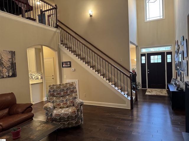 foyer entrance featuring arched walkways, a high ceiling, baseboards, stairway, and dark wood finished floors