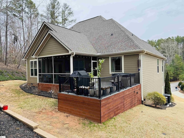 back of property with a sunroom, roof with shingles, and a yard