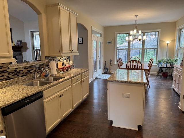 kitchen with arched walkways, a kitchen island, a sink, stainless steel dishwasher, and backsplash