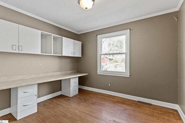 unfurnished office with built in study area, crown molding, baseboards, and wood finished floors