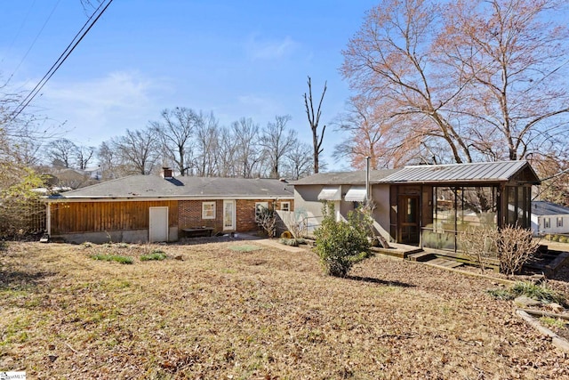 rear view of property featuring a sunroom, a chimney, and brick siding