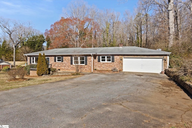 ranch-style home featuring a garage, a chimney, aphalt driveway, and brick siding