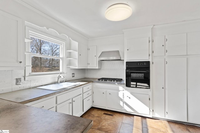 kitchen with stainless steel gas cooktop, a sink, black oven, backsplash, and wall chimney exhaust hood