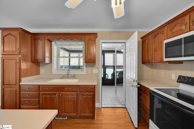 kitchen featuring white microwave, light countertops, light wood-style floors, a sink, and range with electric stovetop