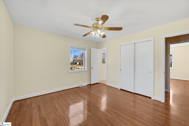 unfurnished bedroom featuring ceiling fan, wood finished floors, visible vents, baseboards, and a closet