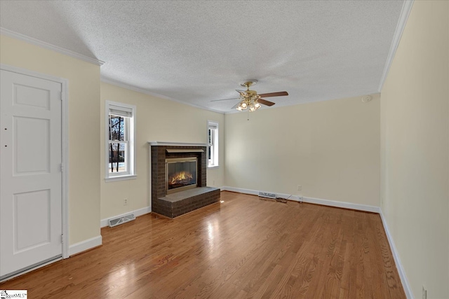 unfurnished living room with a textured ceiling, a fireplace, wood finished floors, visible vents, and ornamental molding