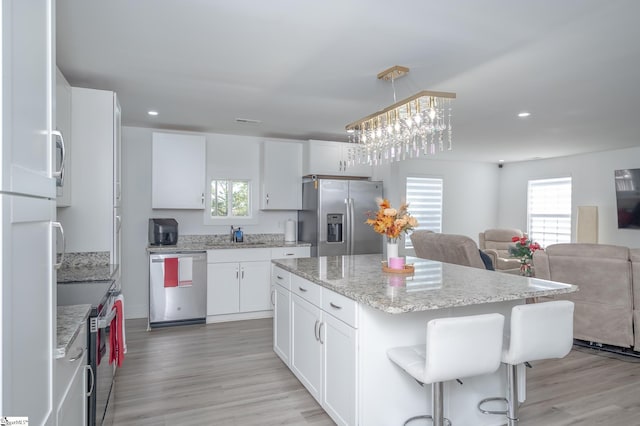 kitchen featuring light wood-style flooring, stainless steel appliances, white cabinets, open floor plan, and a center island