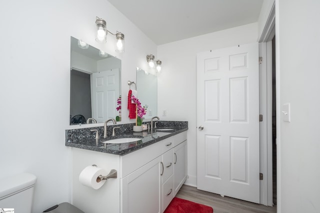 bathroom with toilet, double vanity, a sink, and wood finished floors