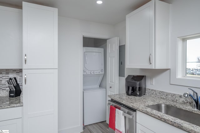 kitchen with white cabinets, dishwasher, stacked washer / drying machine, light stone countertops, and a sink